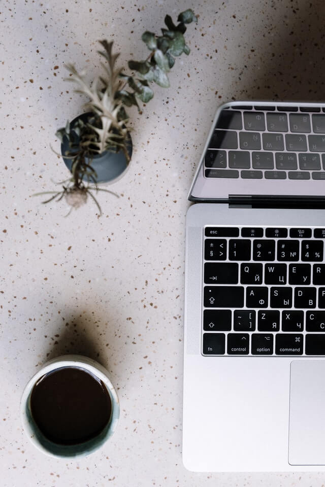 laptop y taza de cafe en un escritorio junto a una planta
